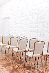Row of festive elegantly gold metal chairs with white cloth indoors hall.
