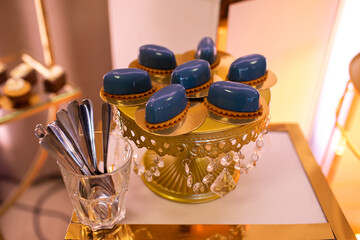 Tasty chocolate cakes with cream mousse and mousse dessert in blue glass glaze on gold stand for party, birthday, valentines day, wedding. Bakery catering. Festive candy bar, buffet sweet bar.