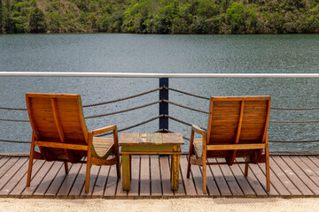 Two empty chairs and small wooden table facing view with beautiful lake and mountains