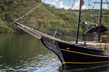 Close up of black boat (schooner) sailing on calm lake with mountains in the background