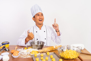 male chef gesturing for ideas using whisk in mixing bowl on table on isolated background
