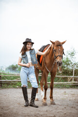 attractive asian cowboy girl standing beside horse on outdoor background