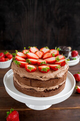 Naked chocolate cake with cream and fresh strawberries on top. Rustic style. Selective focus. Copy space.