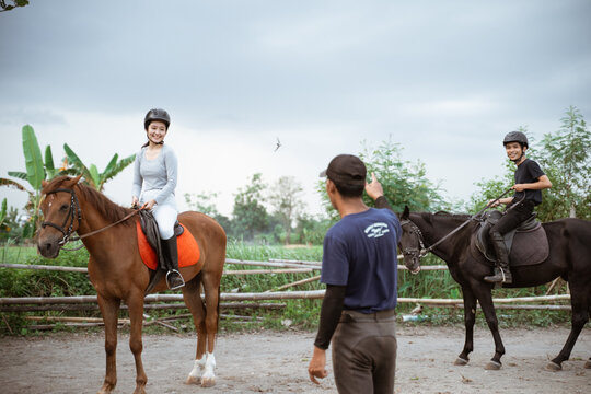 two equestrian athletes riding horses listening to trainer standing guide on outdoor background