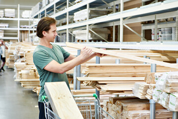 Fototapeta premium Man chooses and buys wooden boards in store
