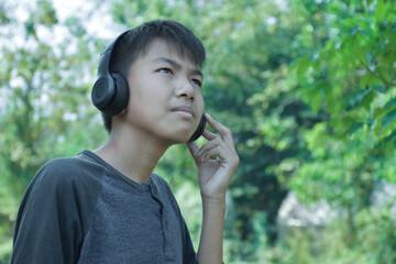 Fototapeta premium Portrait young asian boy holding headphone and listening to music happily in front of the yellow tree during his family vacation in autumn season, soft and selective focus.