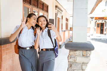 high school asian teenage girls use cell phones for video calls in front of classroom building
