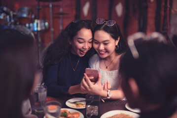 Two friends watching a video on a cellphone while having dinner or eating out in a fancy...