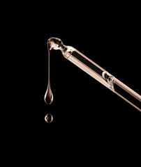 Drops dripping down from cosmetic pipette closeup on a black background