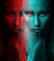 Beautiful woman studio portrait in red and blue color split effect. Model with make-up and dreadlocks holding bird feathers near her face and looking to camera. Futuristic looking style