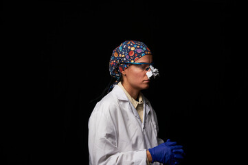 Female doctor in a white coat, blue nitrile gloves and microsurgery glasses and cap on her head ready to examine a patient