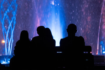 Black silhouette of a family in front of the musical fountain with colourful lights in Budapest,...