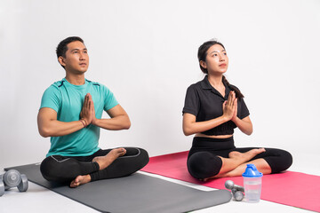 man and woman sitting on mat with hands in front of chest while yoga on isolated background