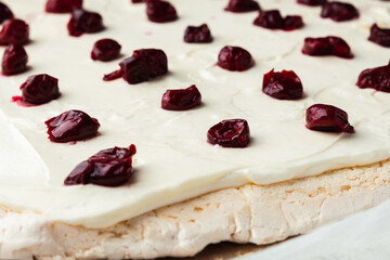 Cut of homemade meringue roll decorated with almond flakes and freeze-dried red cherries on the white marble background. Meringue roulade with whipped cream on a parchment paper