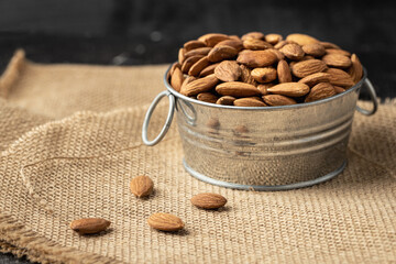 Metal bowl full of almonds on a sackcloth. Pile of nuts stacked together randomly on the burlap background. Healthy nutrition concept