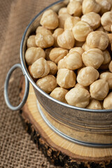 A pile of peeled hazelnuts in a metal bowl on the burlap background Healthy nutrition concept. Traditional rustic agricultural background