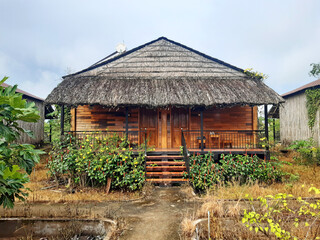 Fototapeta na wymiar Wooden bungalow with a thatched roof in a rustic Mekong setting. Rustic oriental house among tropical vegetation. Thatched roof. Architecture and details of Asian huts.