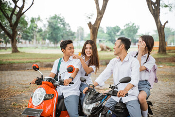 Four students in high school uniforms joking while riding a motorbike on the road