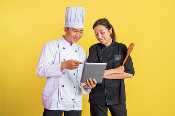 male and female chefs wearing chef jackets using a pad together on isolated background