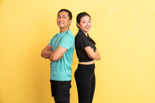 asian man and woman smiling standing back to back on yellow background