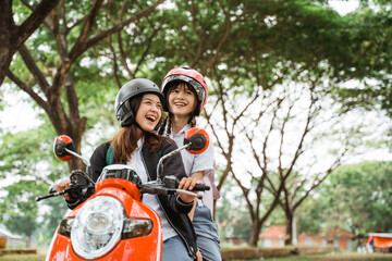 Two student girls wearing helmets and jackets chatting while riding motorbikes together