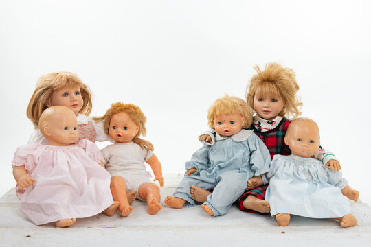 Collection of multiple dolls sitting on a rough white wooden table isolated on white with copy space