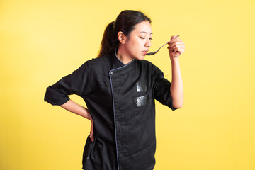 asian female chef using spoon while tasting food while standing on isolated background
