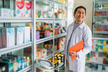 male pharmacist in uniform looking up while holding clipboard standing next to display case