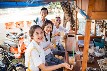 group of high school students in uniform smiling at the camera while drinking ice at a stall