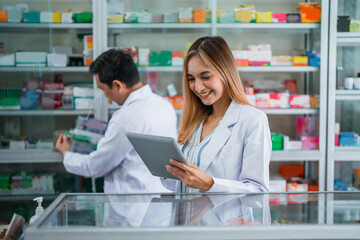 Obraz premium Asian female pharmacist in uniform working using digital tablet in pharmacy