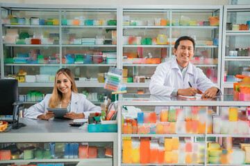 male pharmacist writing and female pharmacist holding pad working behind pharmacy display case