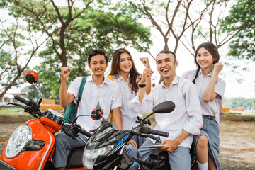 Fototapeta na wymiar Happy high school students with clenched fists celebrating graduation on motorbike