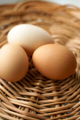 Three chicken eggs of different colors and different sizes lie in a wicker basket