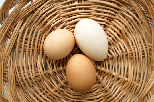 Three chicken eggs of different colors and different sizes lie in a wicker basket