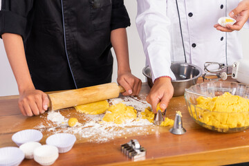 close up of hands of two chefs making cookie dough with utensils on table