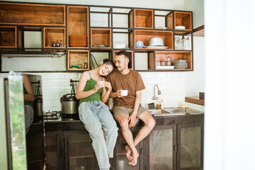 Asian woman and man chatting romantically while drinking coffee using cups in the kitchen background