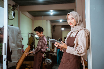 smiling craftswoman in veil holding a tablet stands at the door of the workshop