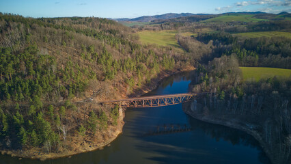 Fototapeta na wymiar Aerial view of steel underspanned suspension railway bridge over Bobr River in Pilchowice, Wonderfull lake with islands and green forests in mountains on a early spring day in Pilchowice, Poland