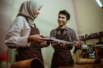 craftsman and craftswoman wearing hijab holding leather products in a leather workspace