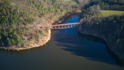 Aerial view of steel underspanned suspension railway bridge over Bobr River in Pilchowice, Wonderfull lake with islands and green forests in mountains on a early spring day in Pilchowice, Poland © Robert