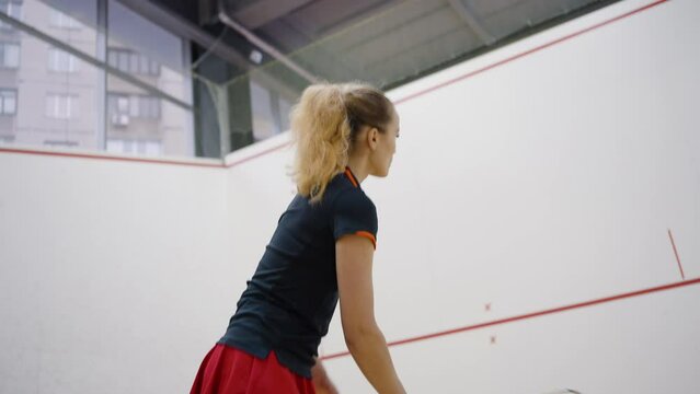 Woman in red tennis skirt trains hitting ball with racket