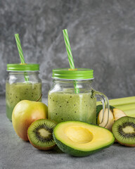 A healthy green smoothie made from fresh vegetables and fruits, on a dark background. Detox drinks from avocado, kiwi, apple, celery in stylish glass glasses. Proper nutrition and healthy lifestyle