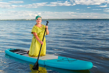 A Jewish woman in a Kisui Rosh headdress on a kneeling SUP board floats on the lake.