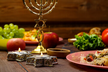 Burning candles in candlesticks Star of David on Shabbat Traditional Jewish food on the laid table, fruits, menorah.