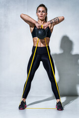 Sports girl doing exercise with kettlebell tied with resistance band on grey background. Strength and motivation
