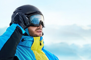 Close Up Of The Ski Goggles Of A Man With The Reflection Of Snowed Mountains. Man In The Background Blue Sky.  Winter Sports.