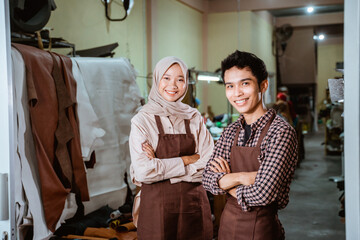 hijabi craftswoman and craftsman smiling with crossed hands in a leather tanning workshop