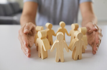 Man wraps two hands around wooden figurines of people standing in circle on table. Concept of...