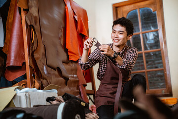 smiling craftsman holding a leather belt in a tannery workshop