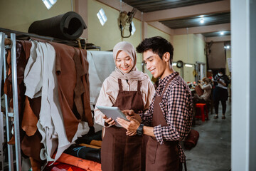 hijabi craftswoman and craftsman using a tablet together in a leather tanning workshop